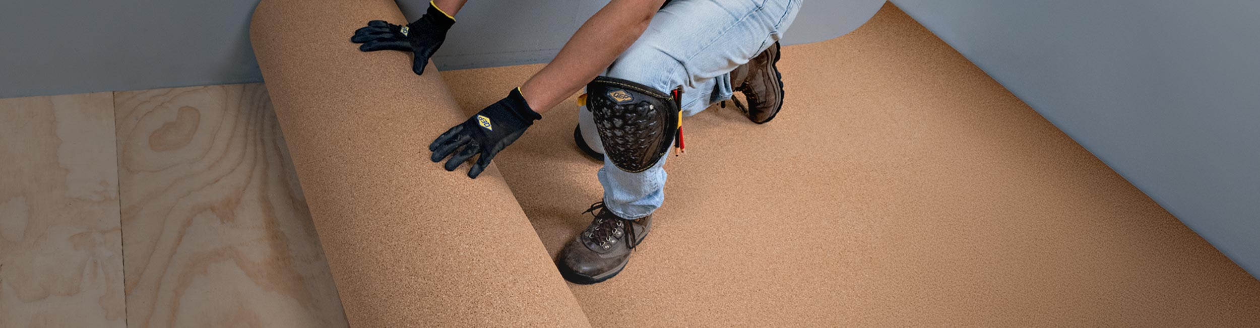Installer rolling out QEP's Natural Cork Underlayment over plywood subfloor for flooring installation