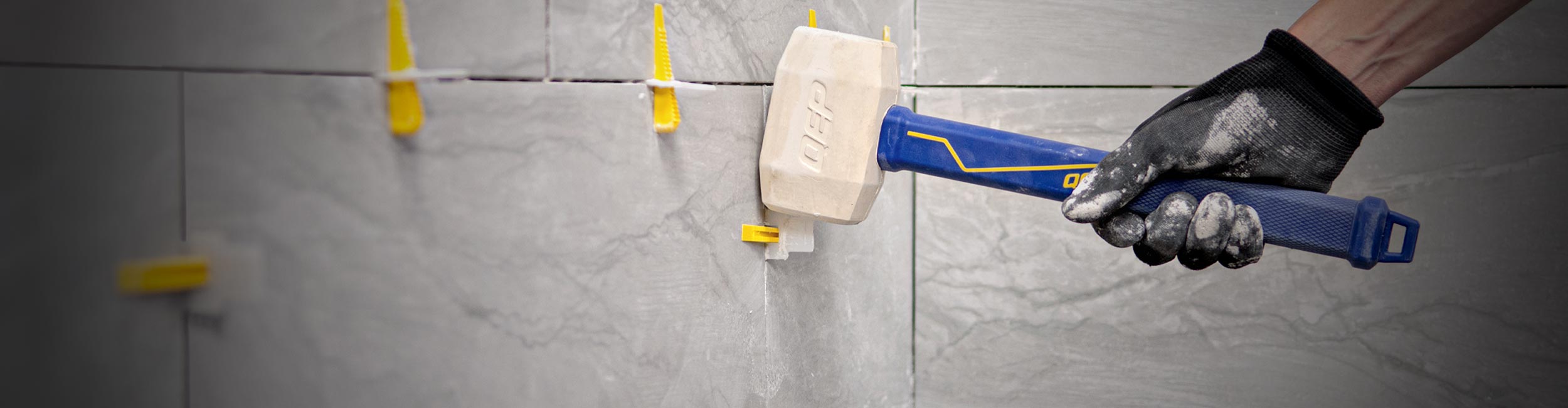Close-up of hand using QEP's Tile Mallet to remove tile leveling clips and wedges during installation
