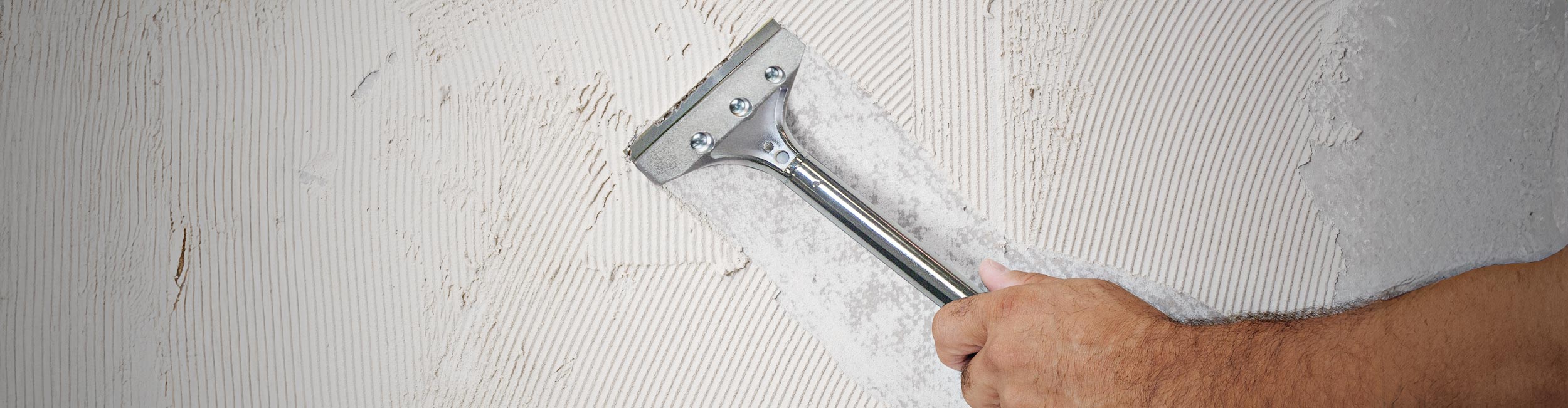 Close-up of a professional installer using a QEP 7" Heavy Duty Floor Scraper to remove old tile and excess debris during demo / tear out