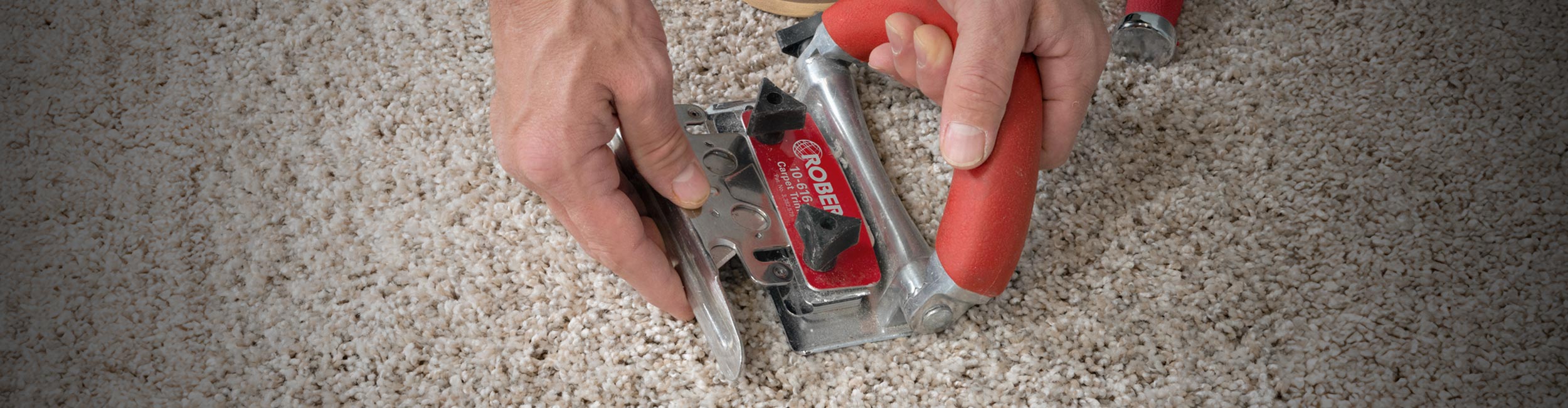 Close-up of an installer using a ROBERTS Conventional Carpet Trimmer to neatly trim carpet along the wall during installation