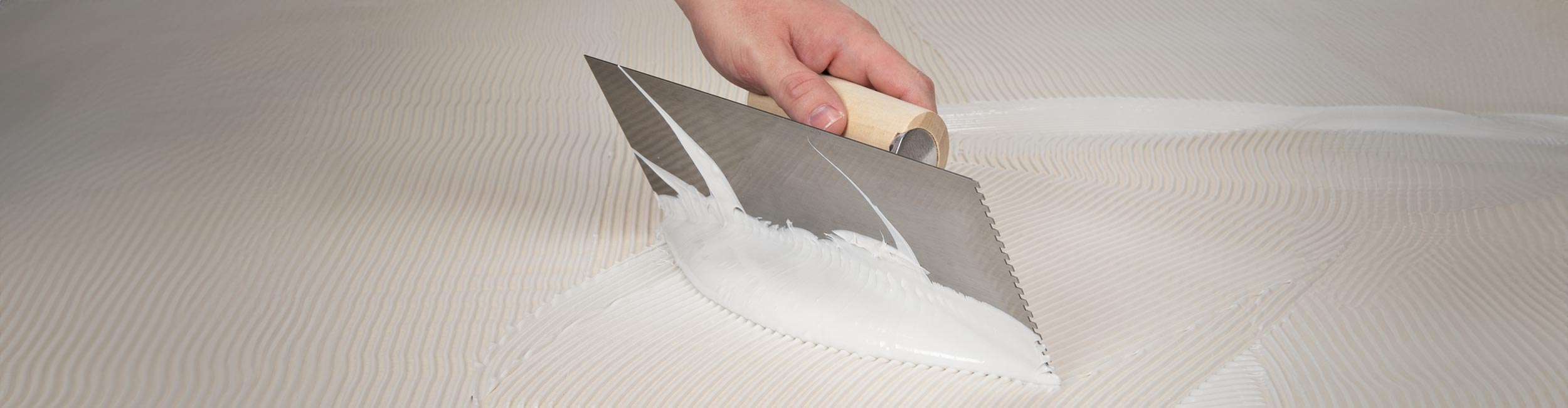 Installer using notched trowel to spread out adhesive evenly across a floor surface