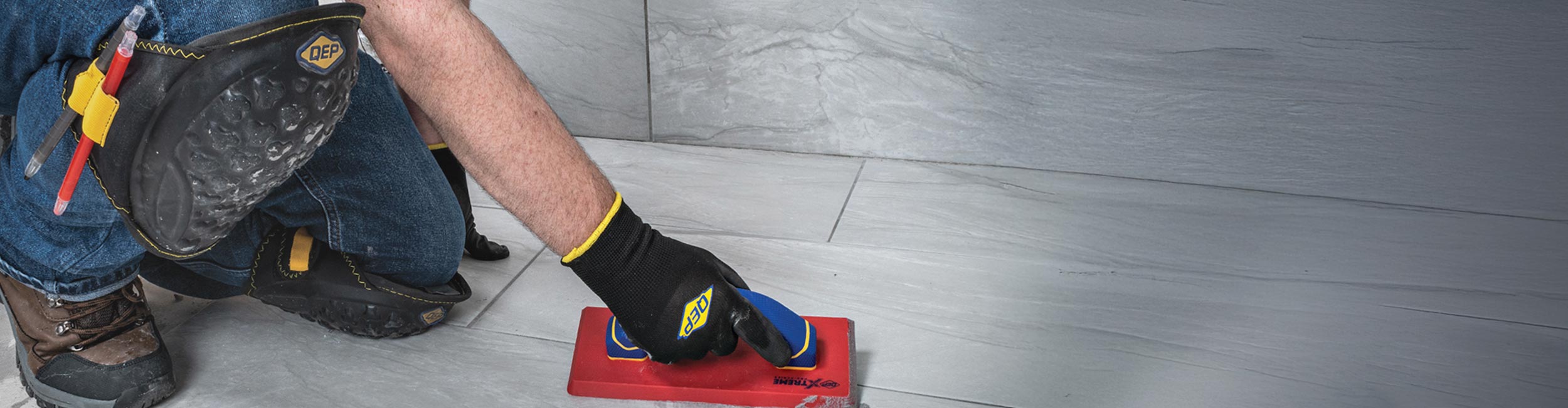 Person wearing QEP's SureGrip Tiler's Gloves and ProMAX Gel Knee Pads during tile installation