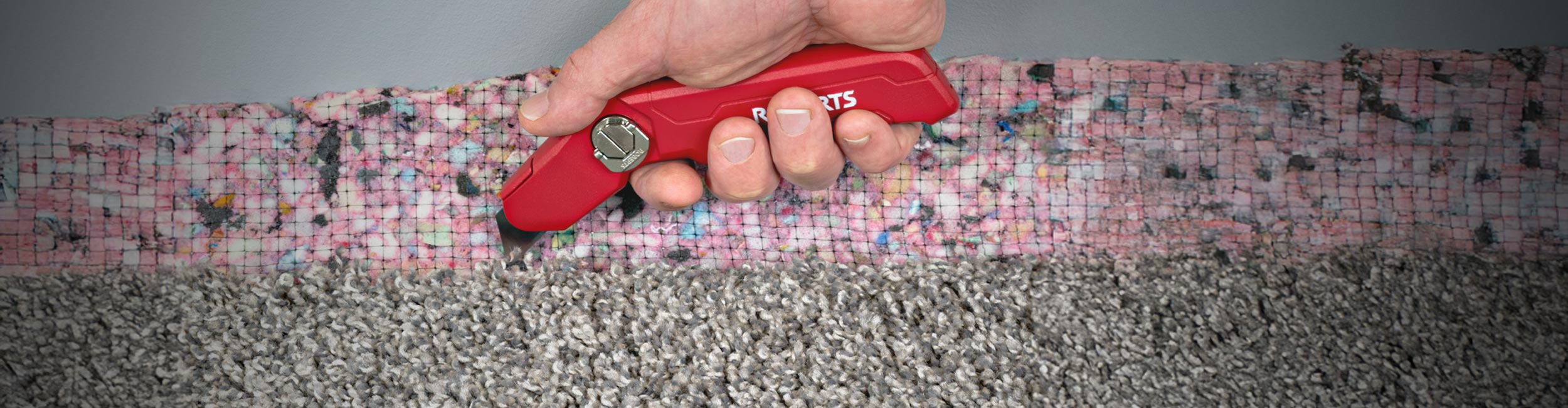 Close-up of hand using ROBERTS Pro Dual-Depth Carpet Knife to cut carpet padding