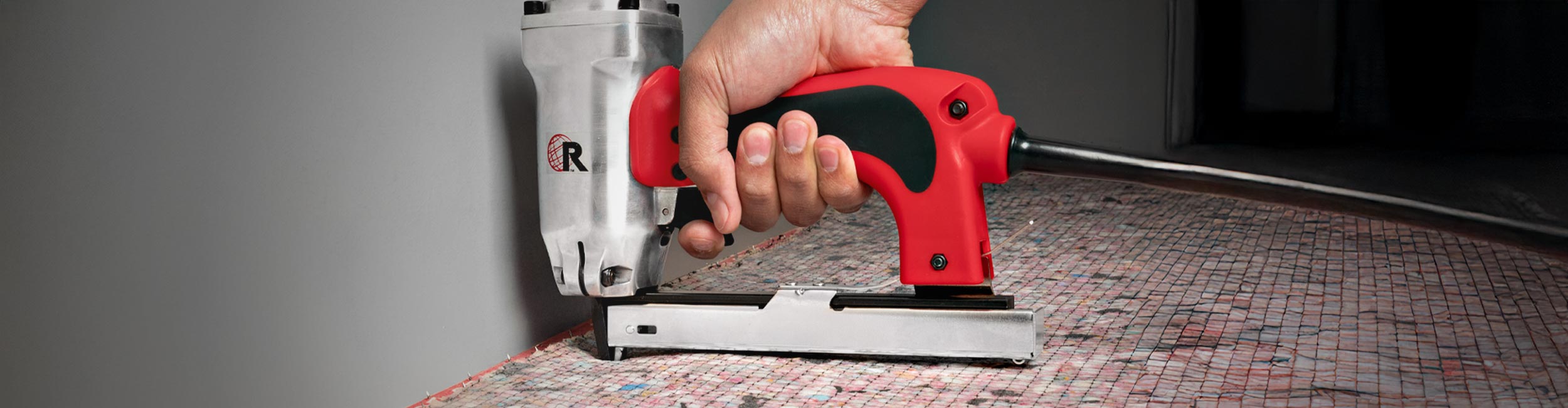 Close-up of hand using ROBERTS Electric Carpet Stapler to tack down carpet padding during install