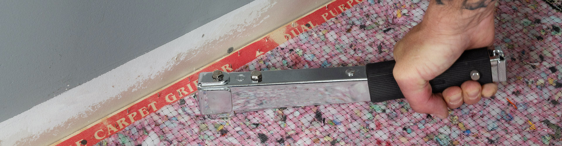A carpet installer using a ROBERTS staple hammer to tack carpet pad near Carpet Gripper tack strip
